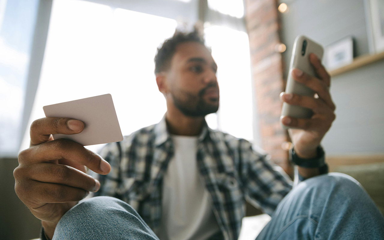 Foto av en mann med betalingskort og mobiltelefon i hånda