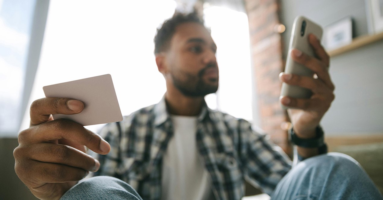 Foto av en mann med betalingskort og mobiltelefon i hånda